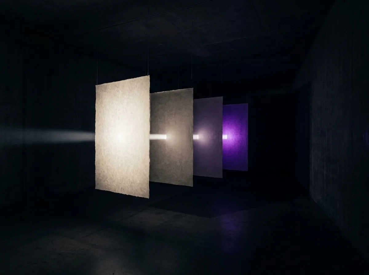 Quatre panneaux de papier translucides suspendus en rang, chacun traversé par un faisceau de lumière.